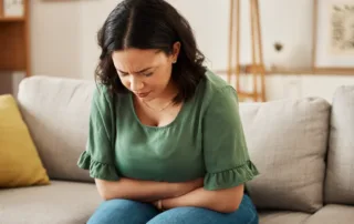 Person sitting on couch holding stomach, showing signs of Mounjaro-related constipation