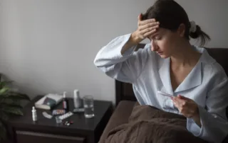 Person sitting in bed checking temperature with medicines and water on bedside table, representing possible health concerns like anemia linked to Ozempic use.