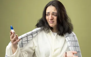 Young woman looking nauseous in robe, holding Ozempic pen, representing common side effect before relief.